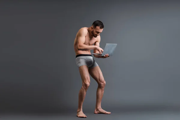 Shirtless and stooped man in boxer shorts using laptop on grey — Stock Photo
