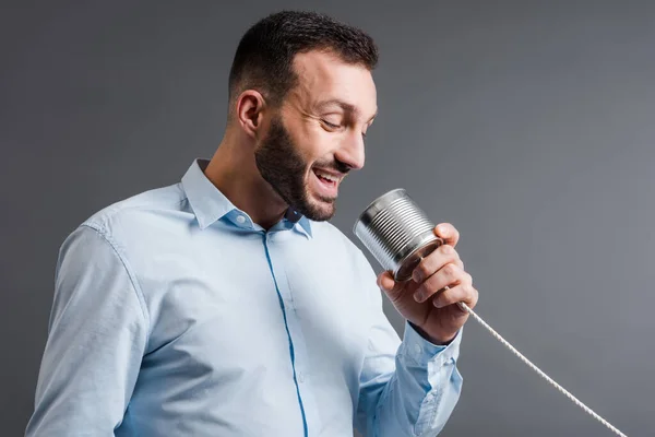 Glücklicher bärtiger Mann im Gespräch, während er Blechdose isoliert auf grau hält — Stockfoto