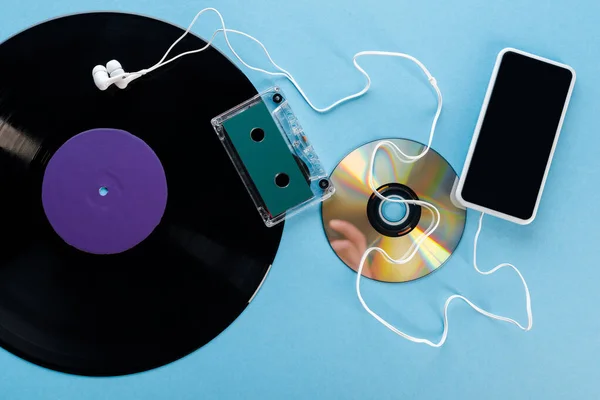 Top view of vintage vinyl record, compact disk, earphones, audio tape and smartphone with blank screen on blue, evolution concept — Stock Photo