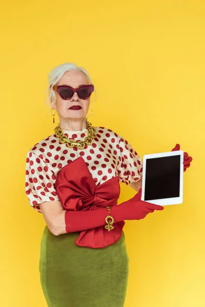 Femme âgée élégante tenant un comprimé numérique isolé en jaune — Photo de stock