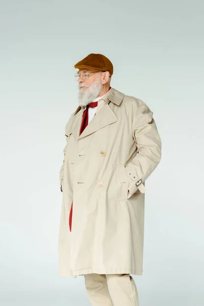 Bonito homem idoso em casaco de trincheira e óculos olhando para longe isolado em cinza — Fotografia de Stock