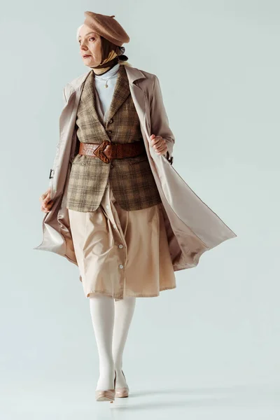 Volle Länge der eleganten Seniorin in Trenchcoat und Baskenmütze auf weißem Hintergrund — Stockfoto