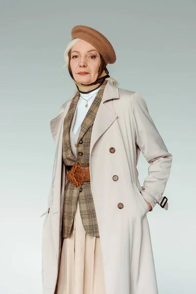 Mulher sênior na moda em boina e casaco de trincheira olhando para a câmera isolada no cinza — Fotografia de Stock