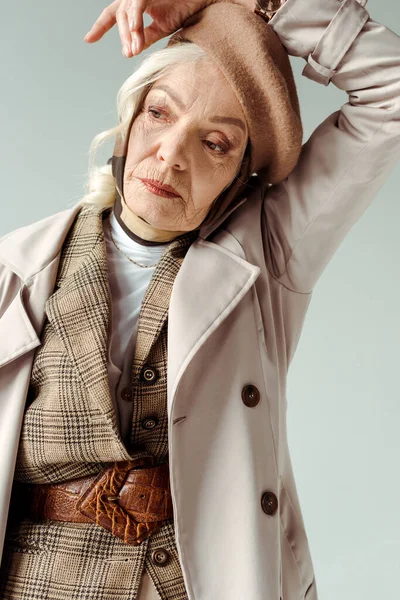 Elegant elderly woman in trench coat and beret posing isolated on grey — Stock Photo