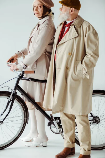 Mulher sênior elegante com bicicleta olhando para a câmera perto de homem bonito no fundo branco — Fotografia de Stock