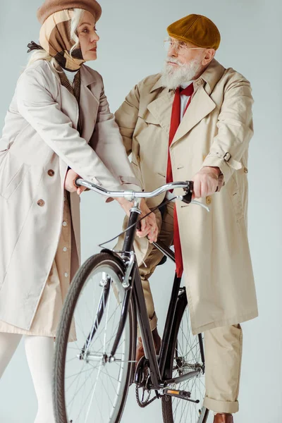 Hübscher Senior sieht Frau im Trenchcoat neben Fahrrad vereinzelt auf grau an — Stockfoto