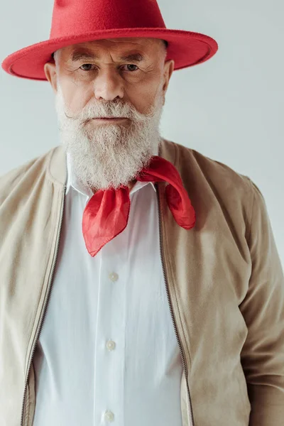 Красивий старший чоловік у червоному капелюсі дивиться на камеру ізольовано на сірому — стокове фото