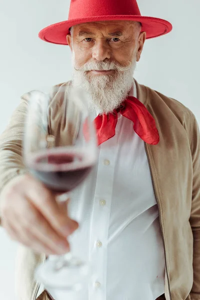 Selektive Fokussierung eines gutaussehenden älteren Mannes mit Hut, der ein Glas Wein in grau hält — Stockfoto