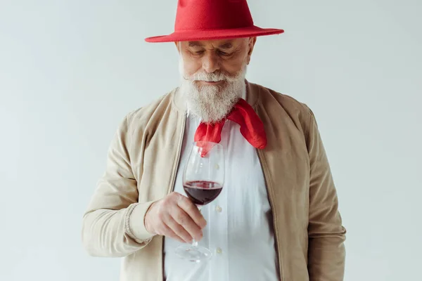 Красивий літній чоловік у червоній шапці тримає келих вина ізольовано на білому — стокове фото