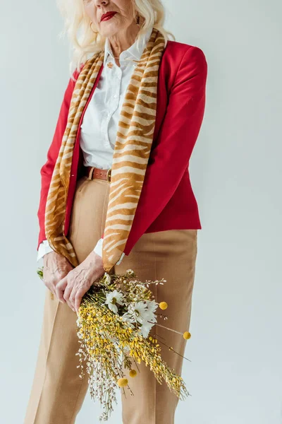 Обрезанный вид стильной пожилой женщины, держащей букет полевых цветов изолированных на сером — стоковое фото