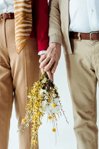 Vista recortada de elegante pareja de ancianos sosteniendo ramo de flores silvestres aisladas en blanco - foto de stock