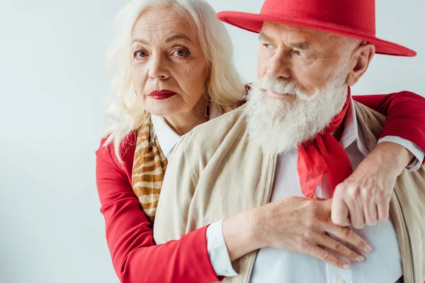 Selektiver Fokus einer eleganten älteren Frau, die in die Kamera blickt, während sie einen hübschen älteren Mann in Weiß umarmt — Stockfoto