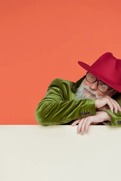 Hombre anciano de moda en sombrero rojo mirando hacia otro lado sobre fondo blanco aislado en coral - foto de stock