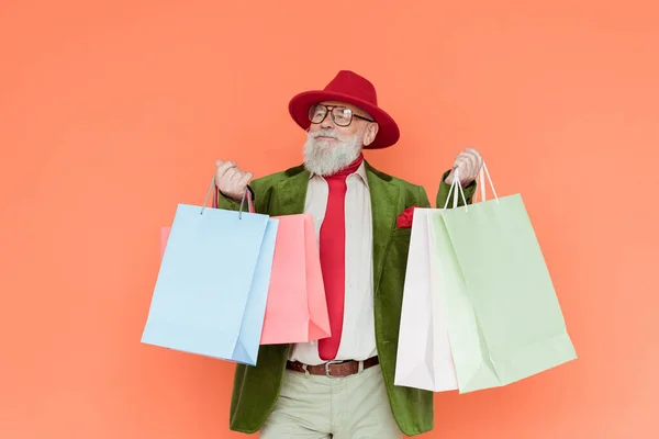 Fashionable elderly man holding shopping bags isolated on coral — Stock Photo