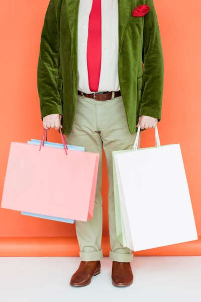 Vista recortada del hombre mayor sosteniendo bolsas de compras en la superficie blanca sobre el fondo de coral - foto de stock