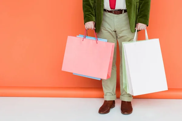 Cropped view of fashionable elderly man holding shopping bags on white surface on coral background — Stock Photo
