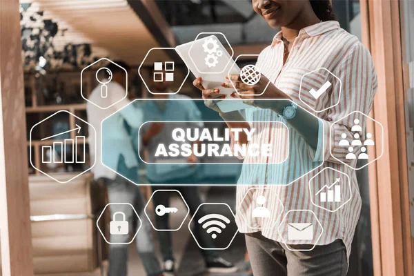 Visão cortada de empresária afro-americana usando tablet digital perto de colegas multiculturais, ilustração de garantia de qualidade — Fotografia de Stock