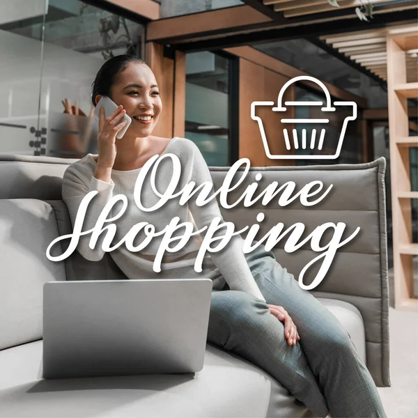 Alegre asiático mujer de negocios hablando en smartphone mientras está sentado en sofá cerca de portátil, ilustración de compras en línea - foto de stock