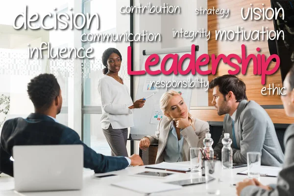 Attractive african american businesswoman standing near flipchart with infographics while multicultural colleagues sitting at desk, leadership illustration — Stock Photo