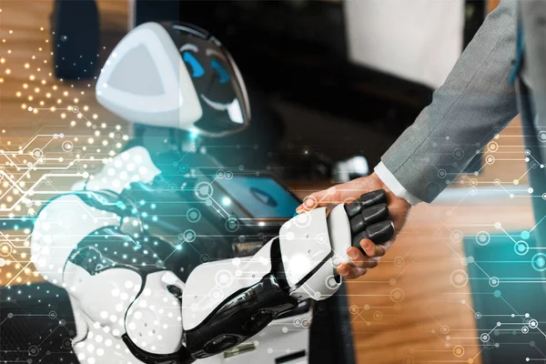 Cropped view of businessman shaking hands with smiling robot in office — Stock Photo