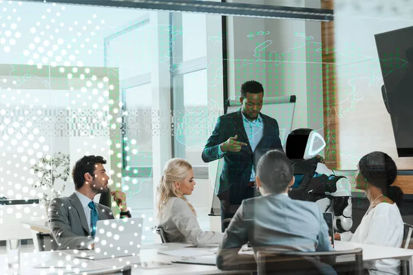 Belo empresário afro-americano mostrando robô para colegas multiculturais no escritório, ilustração cibernética — Fotografia de Stock