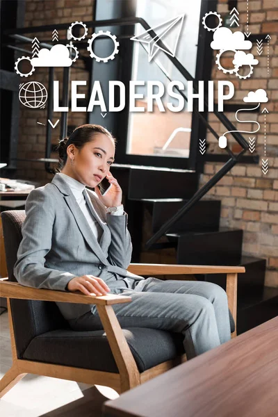Серьезная азиатская деловая женщина сидит в кресле и разговаривает на смартфоне, иллюстрация лидерства — стоковое фото