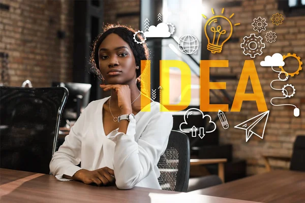 Attractive, thoughtful african american businesswoman sitting at desk and looking at camera, idea illustration — Stock Photo