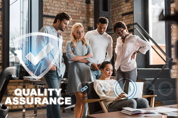 Thoughtful multicultural businesspeople looking at asian colleague working on laptop, quality assurance illustration — Stock Photo