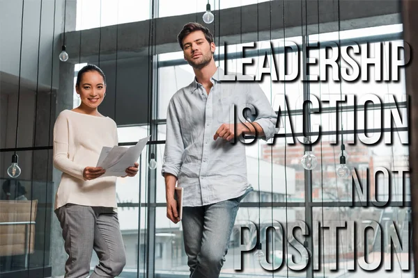 Pregnant asian businesswoman holding papers while standing near handsome colleague, leadership illustration — Stock Photo