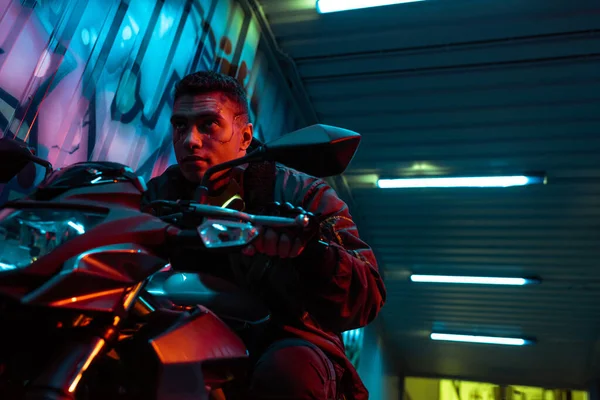 Low angle view of handsome and mixed race cyberpunk player riding motorcycle — Stock Photo