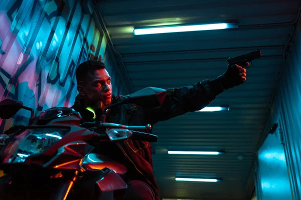 Enfoque selectivo del jugador cyberpunk de raza mixta en el arma de apunte de motocicleta - foto de stock