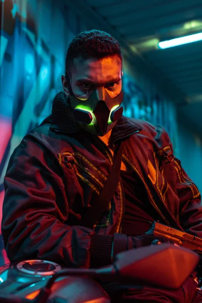 Selective focus of armed mixed race cyberpunk player in protective mask — Stock Photo