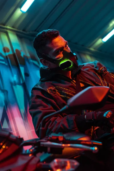 Selektiver Fokus des Mixed Race Cyberpunk-Spielers in Schutzmaske in der Nähe von Motorrädern — Stockfoto