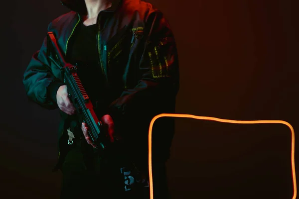 Abgeschnittene Ansicht eines Cyberpunk-Spielers mit Pistole in der Nähe von Neonbeleuchtung auf Schwarz — Stockfoto