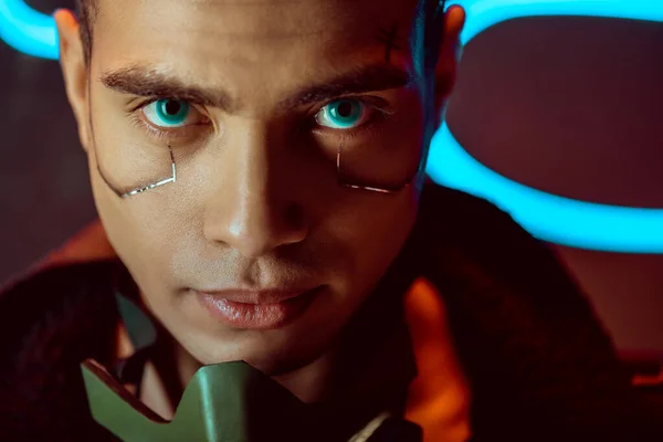 Handsome and bi-racial cyberpunk player looking at camera near neon lighting — Stock Photo