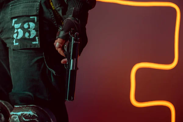 Vista recortada de jugador cyberpunk peligroso con pistola en negro con iluminación de neón - foto de stock