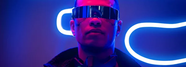 Plano panorámico del jugador cyberpunk de raza mixta en gafas futuristas cerca de la iluminación de neón azul - foto de stock