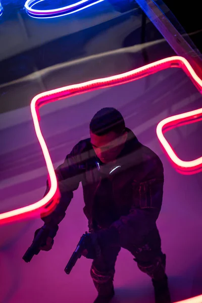 Overhead view of armed mixed race cyberpunk player holding guns near red neon lighting — Stock Photo