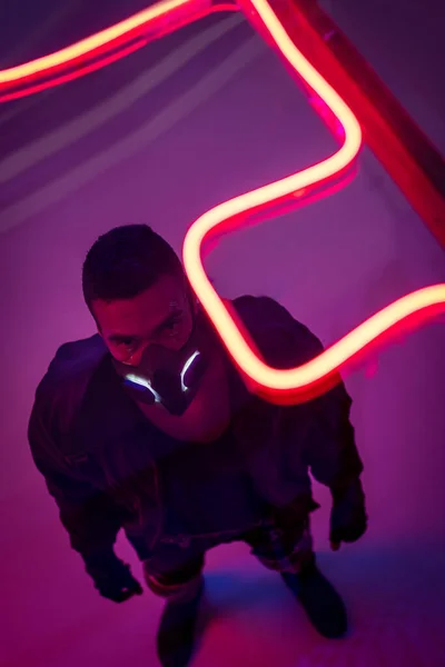 Visão aérea de jogador cyberpunk de raça mista em máscara perto de iluminação de néon vermelho — Fotografia de Stock