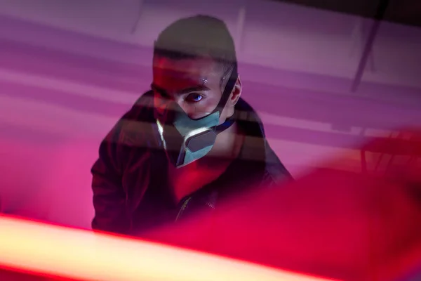 Overhead view of mixed race cyberpunk player in mask looking at camera near red neon lighting — Stock Photo