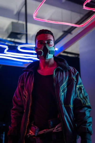 Joueur cyberpunk course mixte dans le masque debout près de néon éclairage — Photo de stock