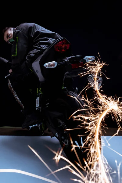 Enfoque selectivo de la raza mixta jugador cyberpunk en la máscara de conducción de la motocicleta con chispas en blanco y negro - foto de stock