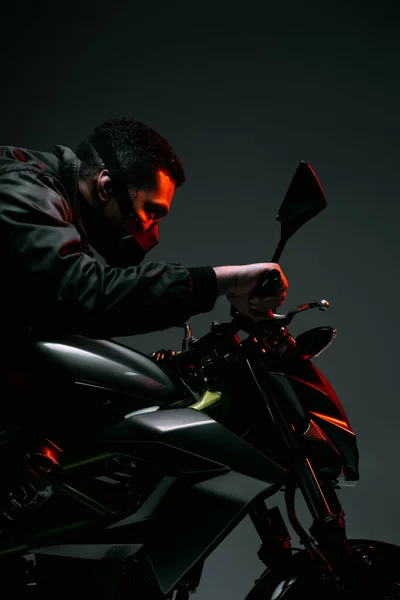 Vista lateral del jugador cyberpunk de raza mixta en la máscara de conducción de la motocicleta en gris - foto de stock
