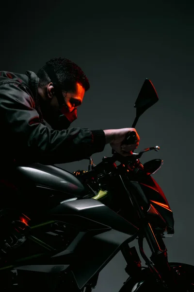 Side view of mixed race cyberpunk player in mask riding motorcycle on grey — Stock Photo