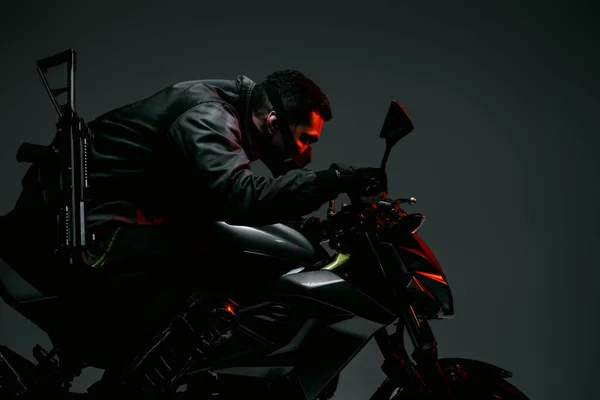 Profile of armed bi-racial cyberpunk player in mask riding motorcycle on grey — Stock Photo