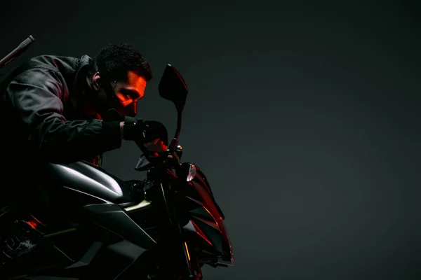 Side view of dangerous bi-racial cyberpunk player in mask riding motorcycle on grey — Stock Photo