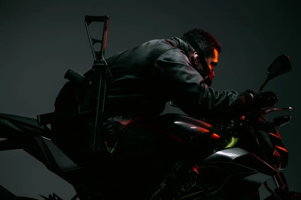 Vista lateral del peligroso jugador cyberpunk de raza mixta en la máscara de conducción de motocicleta en gris - foto de stock