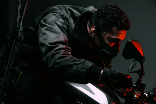 Selective focus of dangerous mixed race cyberpunk player in mask riding motorcycle on grey — Stock Photo