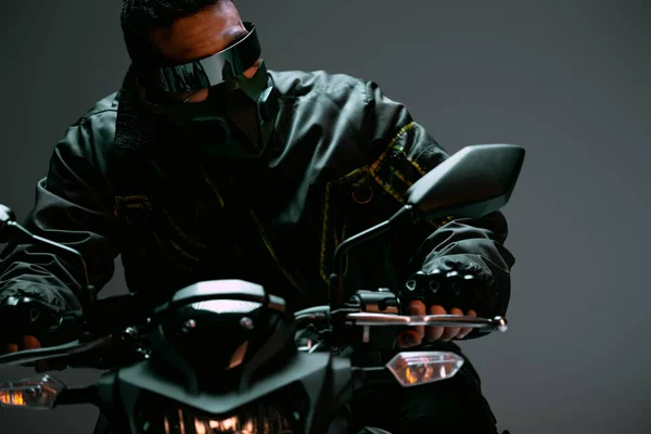Enfoque selectivo de jugador bi-racial cyberpunk en máscara y gafas futuristas a caballo motocicleta en gris - foto de stock