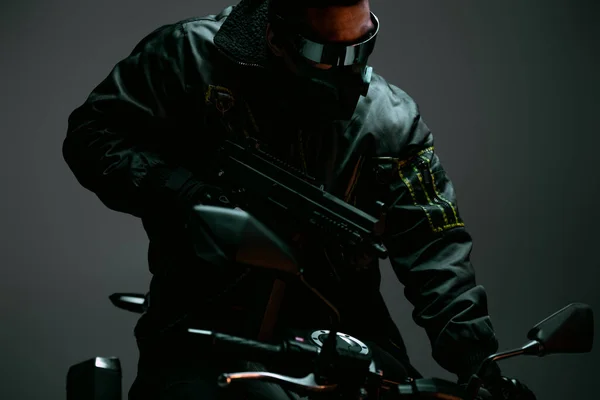 Selective focus of armed bi-racial cyberpunk player in mask and futuristic glasses riding motorcycle on grey — Stock Photo